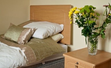 Made bed beside a bedside cabinet with a vase of yellow flowers